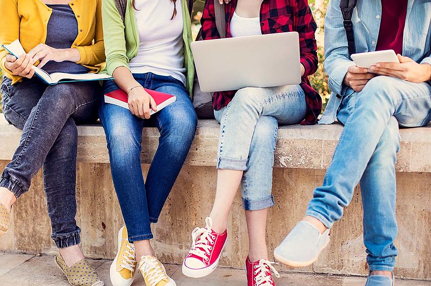 Vier Beinpaare von Jugendlichen, die auf einer Mauer sitzen