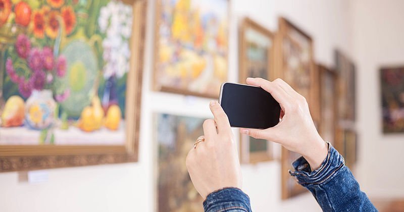 Hände mit Smartphone beim Fotografieren von Gemälden