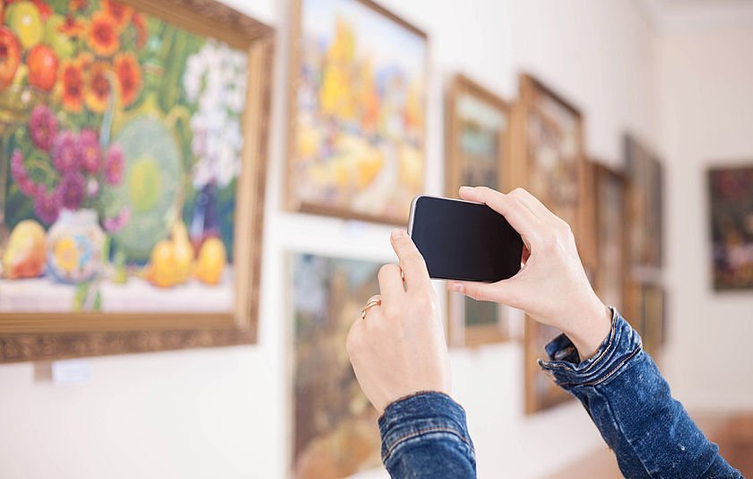 Hände mit Smartphone beim Fotografieren von Gemälden