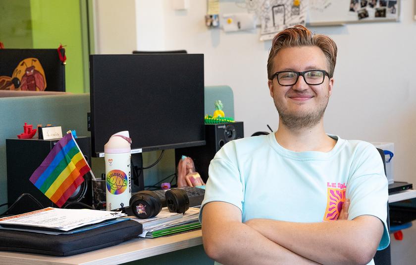 Grinsender Mann mit Brille an einem bunten Arbeitsplatz mit PC