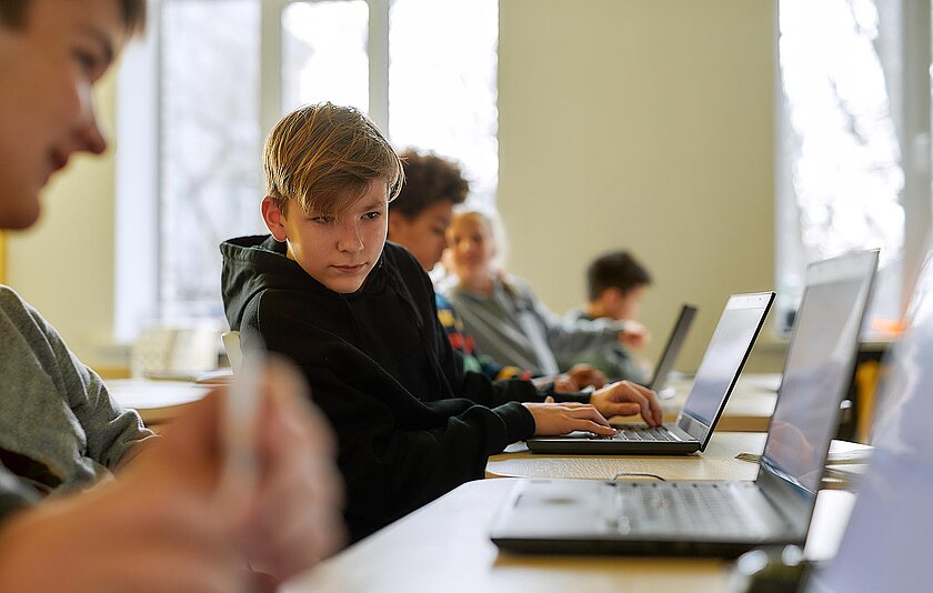 Schüler in Laptop-Klasse schaut zu seinem Nachbarn auf den Bildschirm.