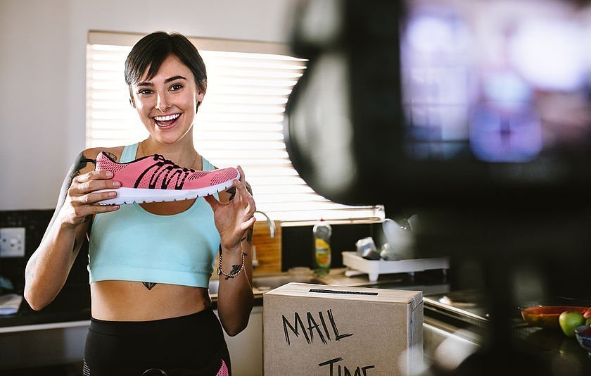 Junge Frau hält einen Sportschuh vor eine Kamera Junge Frau hält einen Sportschuh vor eine Kamera