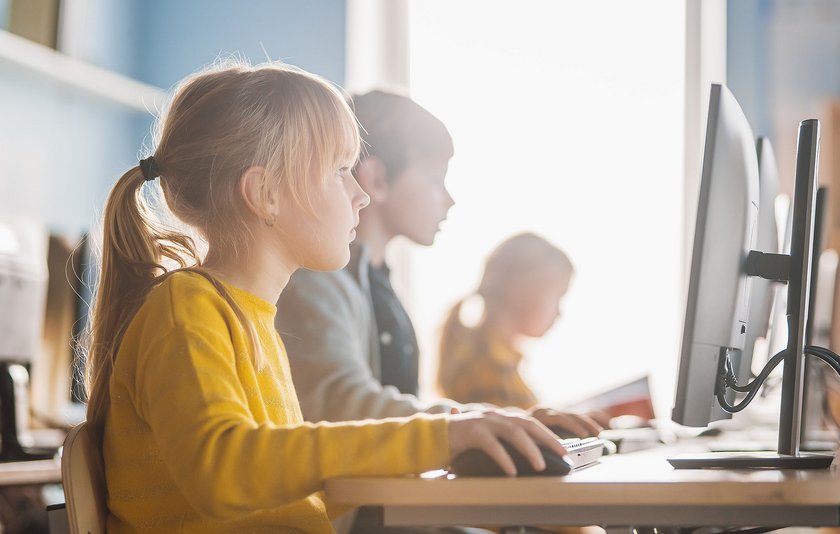 Grundschülerin im gelben Pulli sitzt sehr konzentriert an ihrem PC.