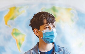 Junge mit Mundschutz vor einer Landkarte