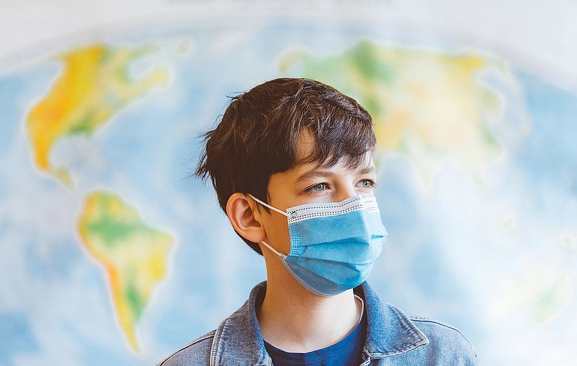 Junge mit Mundschutz vor einer Landkarte Junge mit Mundschutz vor einer Landkarte