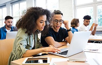 Eine Schülerin und ein Schüler schauen gemeinsam in einen Laptop.