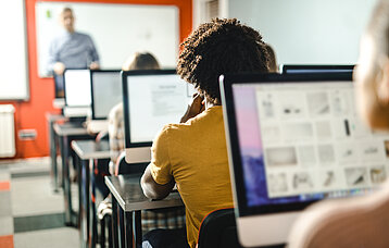 Jugendliche sitzen vor Bildschirmen in einem Klassenzimmer