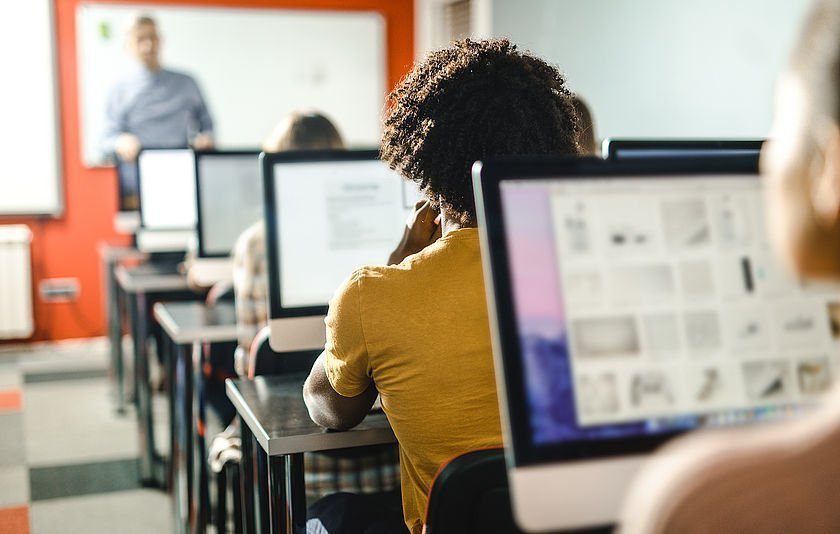 Jugendliche sitzen vor Bildschirmen in einem Klassenzimmer Jugendliche sitzen vor Bildschirmen in einem Klassenzimmer