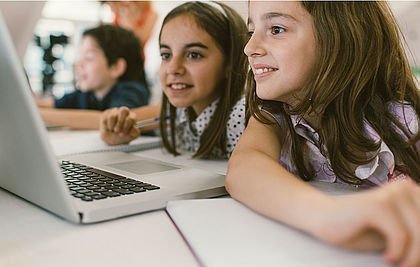 Zwei begeisterte Mädchen schauen in einen Laptop.