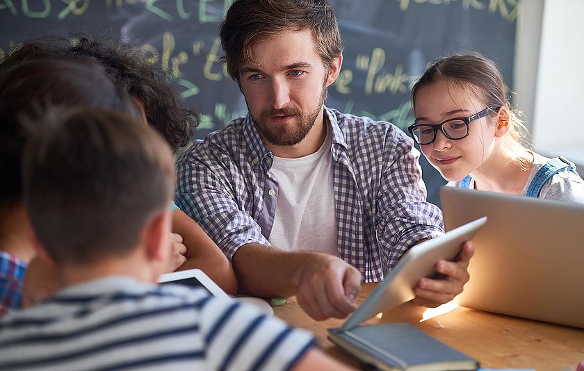 Lehrer mit iPad mit seinen Schülerinnen und Schülern im Unterricht.