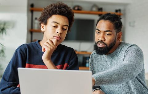 Tipps zu AI Slop für Eltern und Lehrkräfte Ein Vater sitzt mit seinem grübelnden Sohn vor einem Laptop und zeigt ihm etwas.