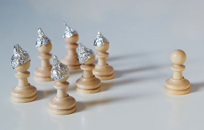 Sieben Schachfiguren, von denen sechs kleine Hüte aus Aluminium tragen.