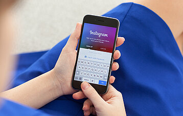 Hände halten ein Smartphone mit Instagram-Startseite