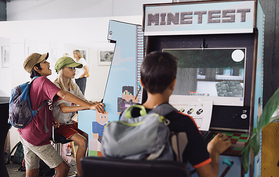 Drei Heranwachsende stehen an Spielautomaten und schauen konzentriert auf den Bildschirm.