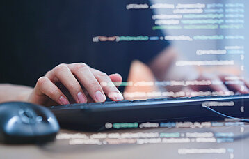 Hände auf einer Tastatur mit eingeblendeter Programmiersprache