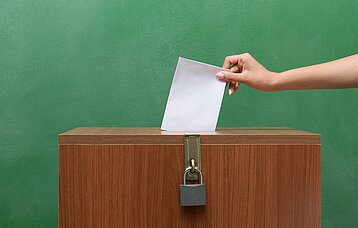 Hand steckt Zettel in eine Wahlurne