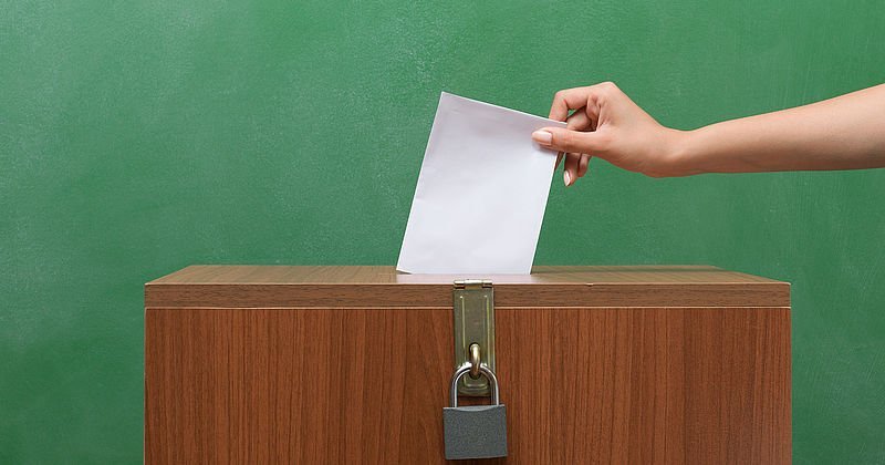 Hand steckt Zettel in eine Wahlurne