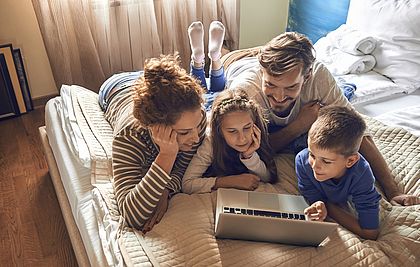 Eine Familie liegt auf dem Bett und schaut gemeinsam in einen Laptop